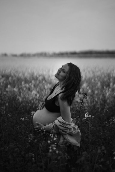 Schwangere Frau in einem Feld, lächelnd und leicht gekleidet, im Schwarz-Weiß.