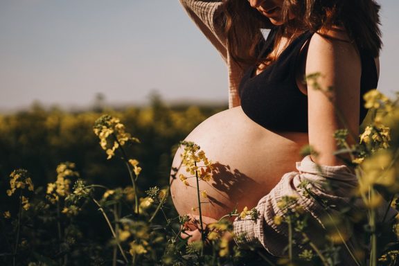 Schwangere Frau streichelt ihren Bauch in einem gelb blühenden Feld.